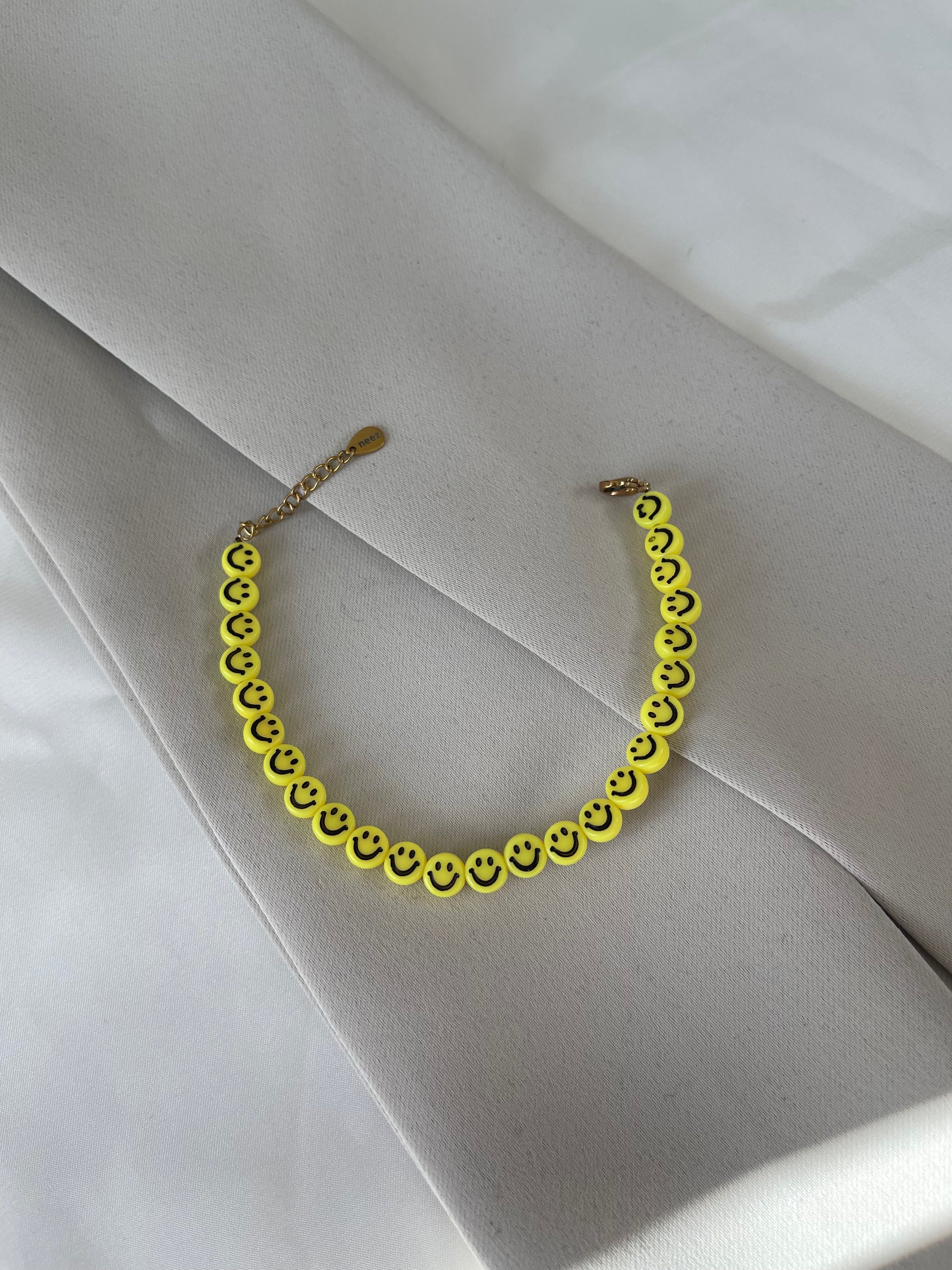 A multicolored bracelet with yellow smiley face charms, placed on a white fabric surface.
