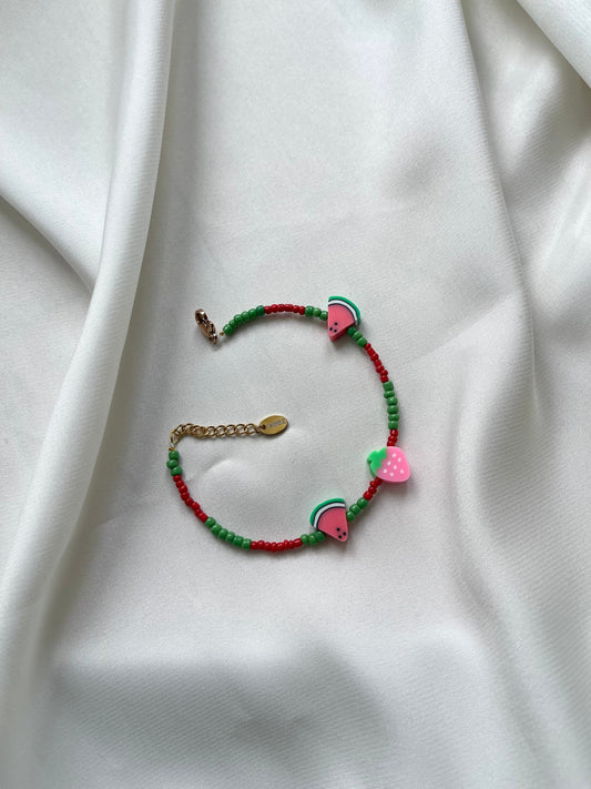 A multicolored bracelet with green, red, and pink beads, featuring a metallic clasp, displayed on a white fabric surface.