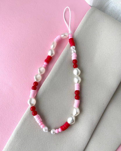 A multicolored phone strap with white, red, and pink beads, placed on a pink background next to a white napkin.