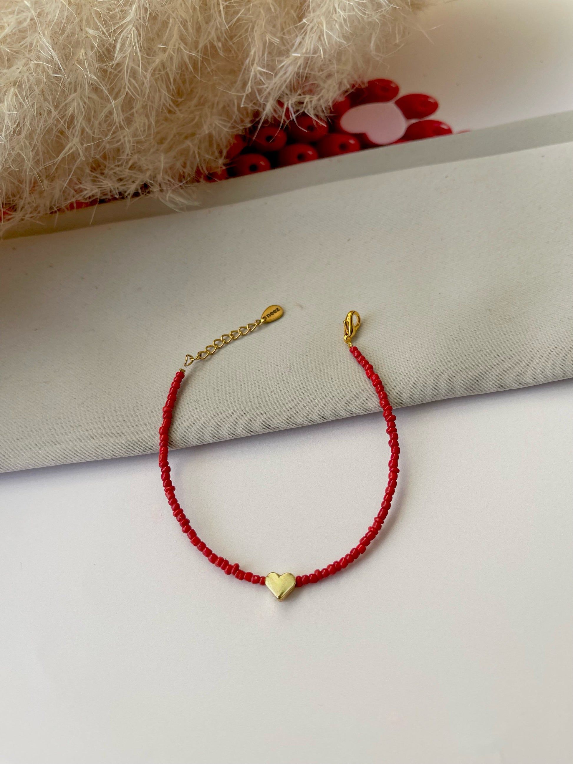 A red bracelet with a heart-shaped charm, displayed on a white surface with a blurred background.