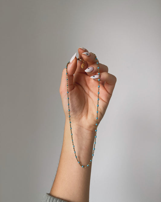A hand holding a blue beaded necklace.